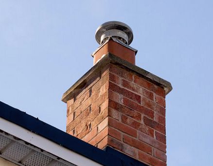 Stainless cap fitted over a clay pot on a corbeled brick chimney