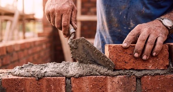 Mason buttering mortar and laying clay brick by hand